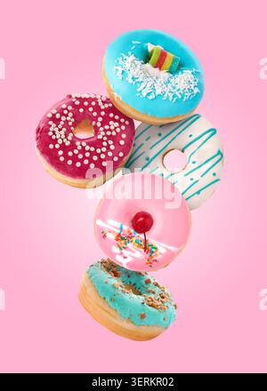 Yummy donuts covered with icing falling on pink background Stock Photo