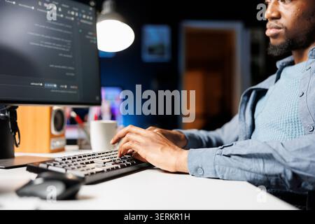 Network administrator functioning via computer programming at home, entering script code for safety and confidentiality; on terminal window, african american technician diagnoses system. Stock Photo
