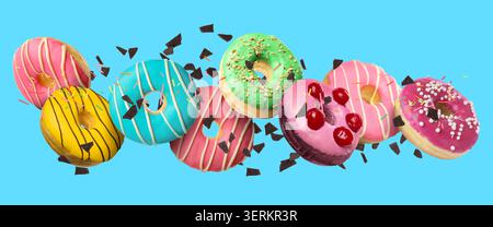 Sweet donuts and chocolate crumbs falling on light blue background Stock Photo