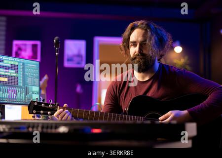 Musician plays acoustic guitar and records melody to compose new song and tunes, computer screen showing DAW software interface with soundtracks, sound engineer in music production Stock Photo