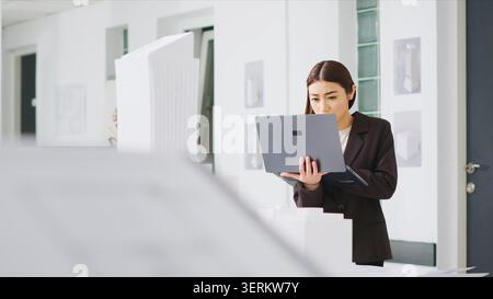 Engineer uses laptop to identify scaling features while observing 3D printed model of a building, real estate agency worker reviewing construction scheme for new development project. Stock Photo