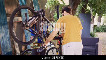 African American female cyclist performing maintenance on damaged bike pedals with assistance from young caucasian man, dedicated people reparing modern bicycle in yard with expert work tool. Stock Photo