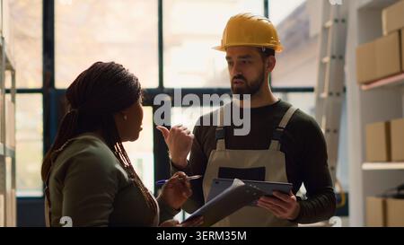 Proficient coworkers performing warehouse inventory controls, discussing ways of keeping quality standards high, qualified experts preparing to ship parcels to customers, crosschecking delivery info. Stock Photo