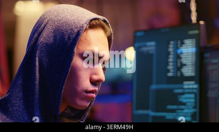 Close-up shot on rogue developer in graffiti sprayed hideaway targeting vulnerable unpatched connections, focused on getting past computer defenses and stealing valuable sensitive data. Stock Photo