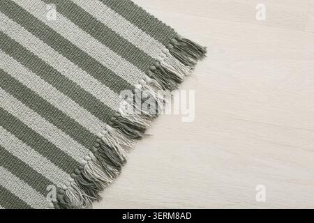 Striped green and white woven fabric with fringed edge on light wood floor background, the textile features a distinct pattern of alternating colors, Stock Photo