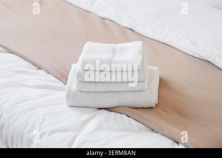 Freshly folded white terry cloth towels stacked on a clean bed with beige blanket, hotel hospitality and spa comfort Stock Photo