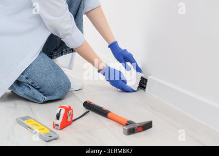 Home renovation and DIY project, woman installing white plastic baseboard trim on wall, construction and interior design Stock Photo