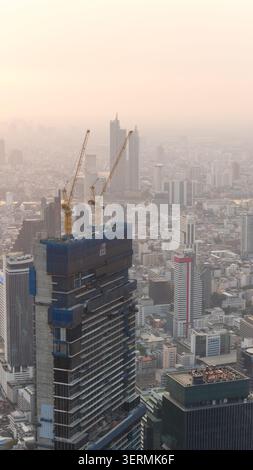 Bangkok, Thailand - 05 February 2026: Aerial view of a skyscraper under construction with two yellow cranes on top overlooking the dense urban skyline Stock Photo