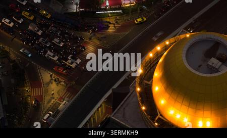 Bangkok, Thailand - 06 February 2026: Aerial view of a busy city intersection at night with heavy traffic and a large illuminated yellow dome structur Stock Photo