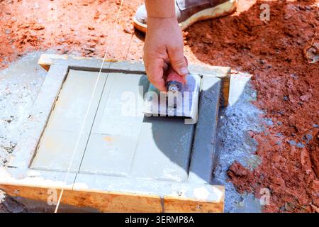 Worker uses trowel to spread edge concrete into wooden mold on construction site Stock Photo