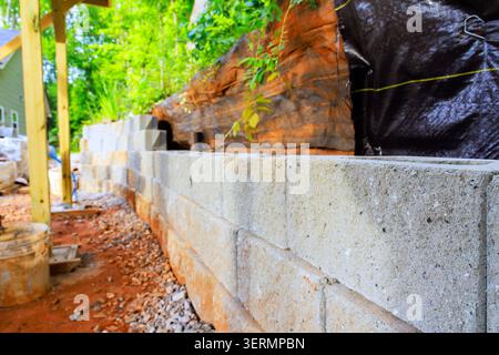 Workers build concrete retaining wall using gray blocks in residential area surrounded construction tools. Stock Photo
