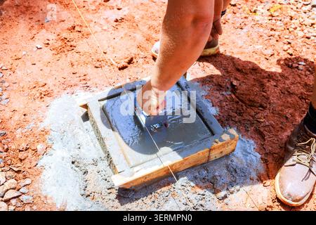 Worker install anchor bracket mixes levels cement in wooden frame at construction site Stock Photo