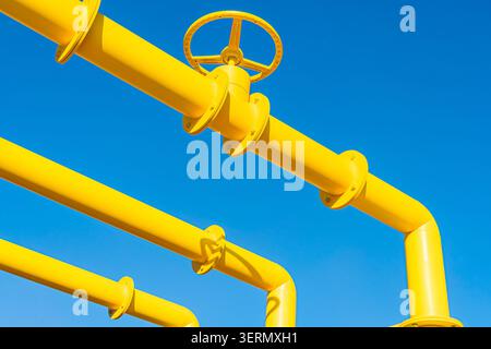 Bright yellow industrial piping connected by flanges, featuring smooth glossy surface, simple functional valve design, contrasting clear blue sky back Stock Photo