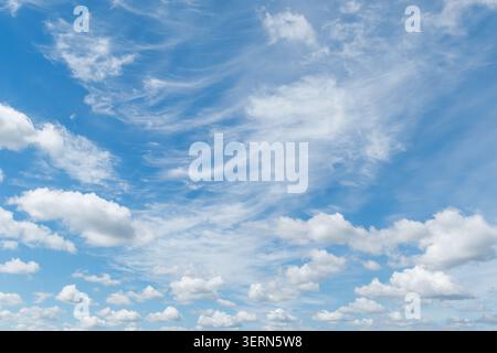 White wispy cirrus and fluffy cumulus clouds scattered over a bright blue sky. Stock Photo