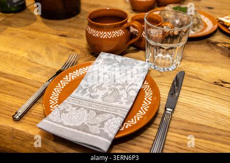 Traditional Lithuanian table setting with ceramic plates, mugs and linen napkin on a rustic wooden dining table indoors. Stock Photo