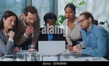 Multiracial business team partners managers looking in laptop with shock amazed wonder reading good online news work success at office meeting Stock Photo