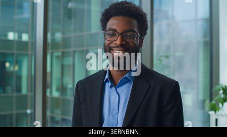 Serious African American business man look away turning looking at camera happy smiling in office. Ethnic confident businessman smile toothy male Stock Photo