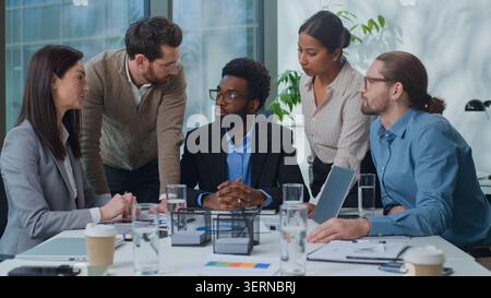 African American businessman boss with multiethnic business team discussing papers stats at office meeting. Five diversity managers talking Stock Photo