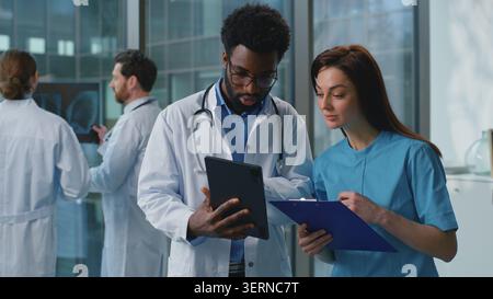 Two diversity doctors man with woman discussing medical examination using digital tablet together in hospital. Caucasian female therapist doctor Stock Photo