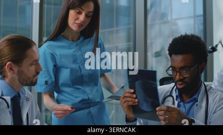 Professional multiethnic medical team of experienced doctors discussing x-ray using digital tablet laptop talking about diagnosis healthcare briefing Stock Photo