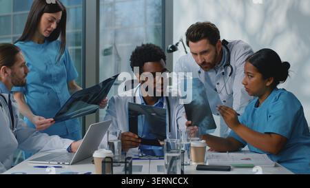 Group team of five multiethnic doctors talking working with x-rays at table at medicine conference. Multiracial medical therapists work with health Stock Photo