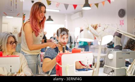 Teacher guiding young man learning sewing machine in workshop Stock Photo
