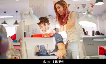 Instructor teaching young man sewing machine operation in workshop Stock Photo