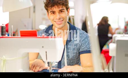 Young tailor smiling while working at sewing workshop Stock Photo