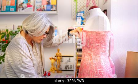 Senior woman creating garment on mannequin in workshop Stock Photo