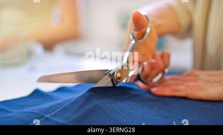 Seamstress cutting blue fabric with scissors in tailoring workshop Stock Photo