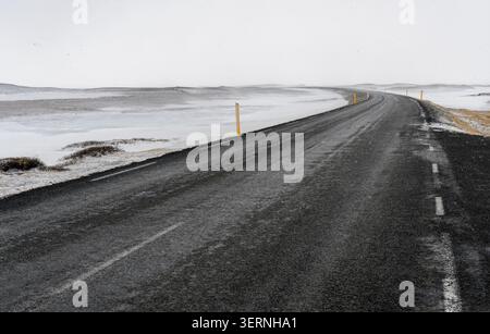 Winding black asphalt road extending through an empty snowy icelandic winter landscape, offering a sense of travel and solitude. Iceland landscape Stock Photo