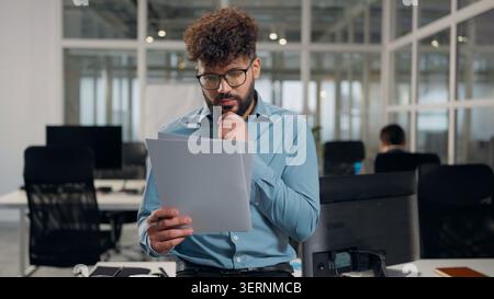 Ethnic Arabian business man working looking in papers report thinking writing notes standing in office guy businessman with diagram result financial Stock Photo