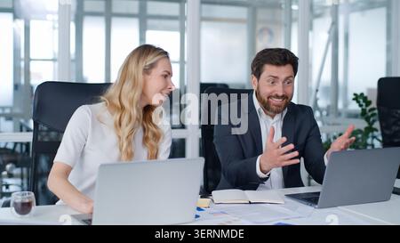 Two business workers win with computer in office. Caucasian businessman showing laptop good result offer businesswoman support rejoicing winning woman Stock Photo