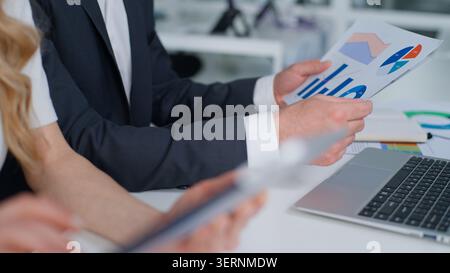 Close up unrecognizable Caucasian business team with paperwork analysing stats at table two unknown coworkers holding papers documents diagrams Stock Photo