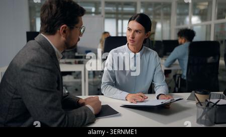 Two Caucasian business office workers discuss papers stats businesswoman talking with businessman consulting intern corporate education trainee mentor Stock Photo