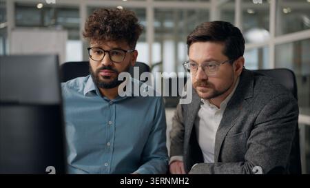 Two multiracial business men talking working computer in office partnership teamwork cooperation multiethnic businessmen males talk work Arabian Stock Photo