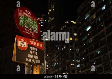A bus stop sign at Arsenal Street in Hung Hom, Hong Kong, at night, listing multiple route numbers against illuminated residential and commercial high Stock Photo