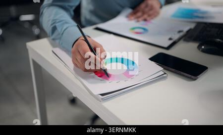 Close up male hands holding pen analyzing circle diagram with profit results datum unknown business man analyst review data stats financial progress Stock Photo