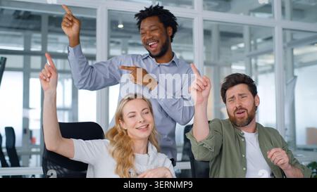 Joyful carefree corporate group business team dancing doing same movement with hands moving having fun clapping palm fooling in office three happy Stock Photo