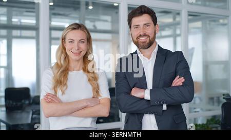 Caucasian business team two colleagues partners posing with crossed hands in office mature businessman with businesswoman smiling happy looking at Stock Photo