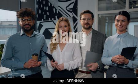 Four successful happy multiethnic business managers posing in office together standing in company marketing corporate workplace group team of Stock Photo