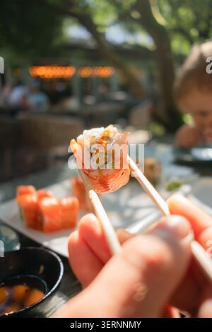 Mouthwatering close-up of fresh salmon and cucumber sushi roll held with chopsticks, showcasing authentic Japanese dining experience. Stock Photo