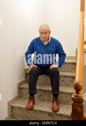 pensive senior man sitting and resting on the stairs of the house Stock Photo