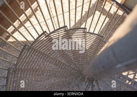 High angle looking down view of a modern industrial spiral staircase made of metal mesh steps. Geometric pattern created by steps and shadows in Stock Photo