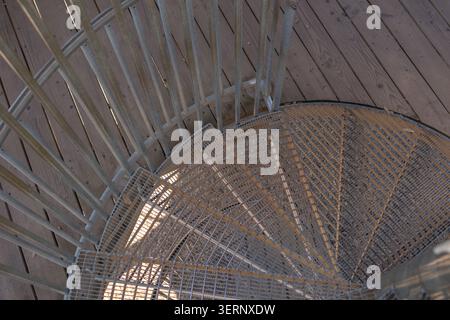 High angle close up shot looking down the entry point of an outdoor spiral metal staircase with railings and wooden deck floor. Architectural details Stock Photo
