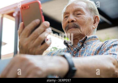 Portrait of happy senior man holding walking stick while using a smartphone at home. Selective focus. Senior health care concept. Stock Photo