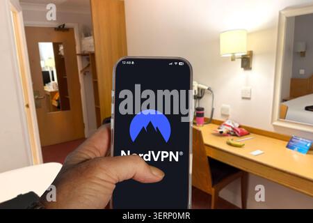 Hand holding an iPhone displaying the NordVPN logo on the screen inside a hotel room Stock Photo