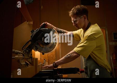 Adult Man Operating Miter Saw in Carpentry Workshop Stock Photo