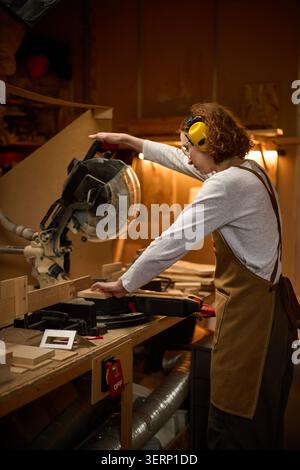 Adult Woman Operating Miter Saw in Carpentry Workshop Stock Photo