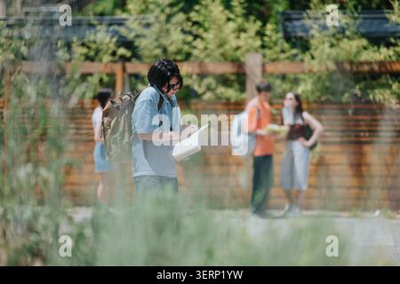 Student writing in notebook on sunny campus lawn while classmates chat in background Stock Photo